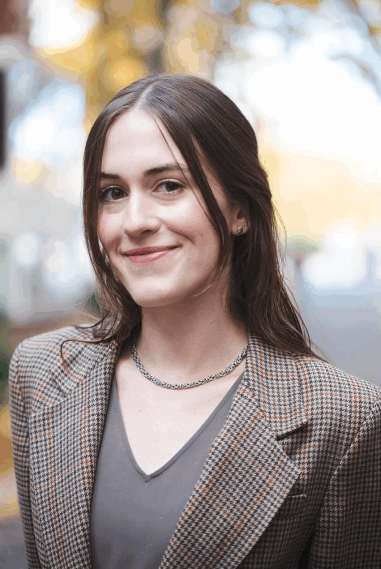 Giulia Neaher in a blazer, smiling outdoors. Headshot of the blogger.
