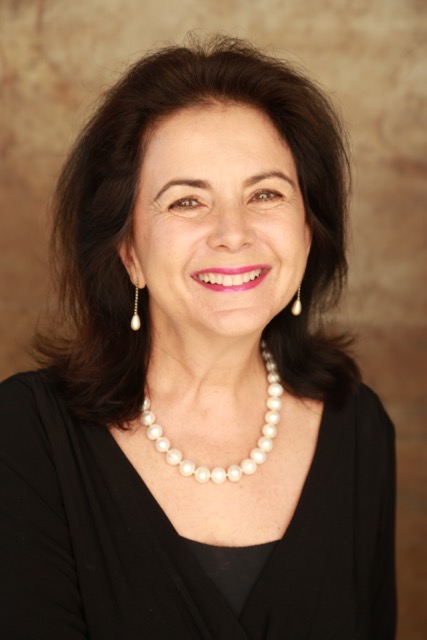 Mary Machado-Schammel portrait, smiling woman with pearl necklace and earrings.