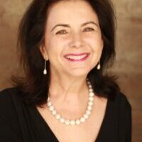 Mary Machado-Schammel portrait, smiling woman with pearl necklace and earrings.